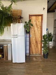 Esse era o antes do ambiente com geladeira branca, porta de madeira e vaso sem suporte.