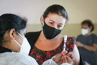 Aplicadora mostrando para mulher que foi se vacinar o imunizante que ela irá tomar. (Foto: Henrique Kawaminami/Arquivo)