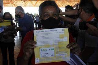 Evanir Ferreira mostra cartão do Mais Social; ao fundo, governador durante entrega. (Foto: Chico Ribeiro)