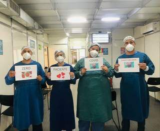 Profissionais da saúde seguram cartazes com os dizeres sobre a falta de pacientes com covid no hospital. (Foto: Cassems/Reprodução)