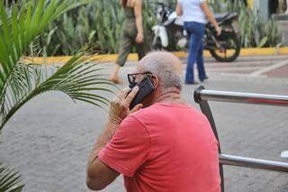 Homem fala ao celular, sentado na Rua 14 de Julho. (Foto: Paulo Francis)