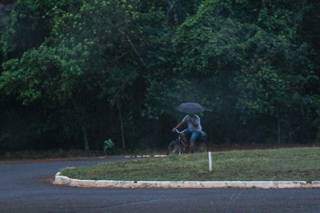 Ciclista precisa se equilibrar ao pedalar e segurar o guarda-chuva no Parque dos Poderes. (Foto: Henrique Kawaminami)