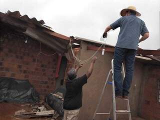 Moradores improvisando cobertura de residência destelhada pelo vendaval. (Foto: Divulgação)