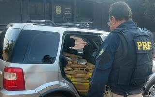 Policial diante dos tabletes de maconha que estavam sendo transportados no veículo. (Foto: PRF)