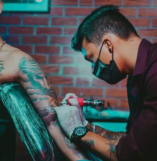 Kadu no estúdio tatuando o braço de um cliente. (Foto: Arquivo pessoal)