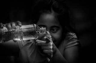 Criança conta gota de água que cai da garrafa. (Foto: Marcos Maluf)