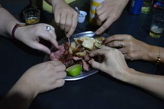 Grupo de pessoas compartilha de prato com váriospedaços de carne. (Foto: Bárbara Cavalcanti)
