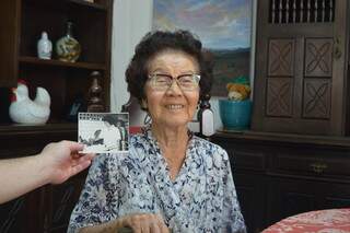 Dona Yakuso Katsuren, de 91 anos, ao lado da fotografia original feita dela preparando sobá. (Foto: Bárbara Cavalcanti)