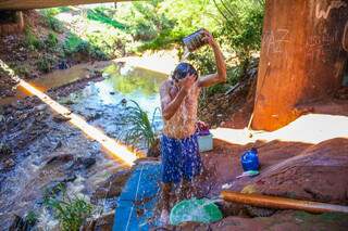 Wiliam Giovan toma banho em um cano improvisado no pontilhão. (Foto: Paulo Francis)
