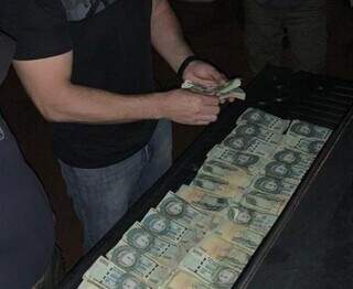 Policial conta dinheiro encontrado enterrado no quintal de suspeito de sequestro. (Foto: Divulgação)