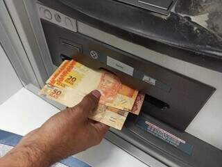 Pessoa sacando dinheiro em caixa eletrônico de banco (Foto: Kisie Ainoã)