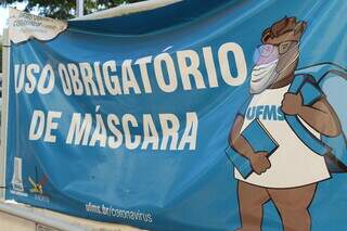 Cartaz em frente a UFMS anuncia obrigação do uso de máscara dentro do câmpus universitário. (Foto: Kísie Ainoã)