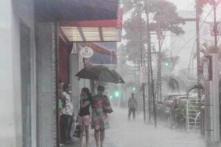 Pessoas se protegendo da chuva na Rua 14 de Julho. (Foto: Marcos Maluf)