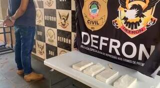 Traficante detido na sede da Defron ao lado dos tabletes de cocaína. (Foto: Polícia Civil) 