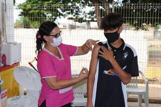 Profissional de saúde prepara braço de menino para aplicar dose da vacina. (Foto: Sesau)