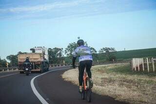 Ciclista pedala no acostamento de rodovia em Mato Grosso do Sul, disputando espaço com caminhão. (Foto: Henrique Kawaminami)