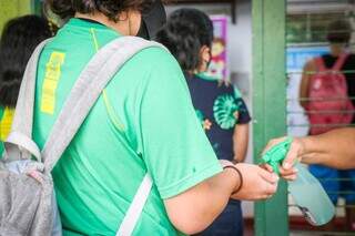 Na porta da escola, funcionária passa álcool nas mãos dos alunos. (Foto: Henrique Kawaminami)