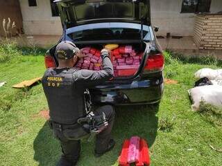 Policial retirando os tabletes da droga do veículo. (Foto: DOF) 