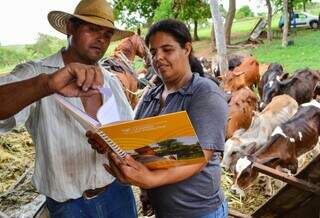 Homem e mulher manuseiam livro do Senar em fazenda de bovinocultura (Foto: Divulgação/Sistema Famasul)