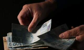 Homem conta notas de dinheiro após efetuar saque (Foto: José Cruz/Agência Brasil)