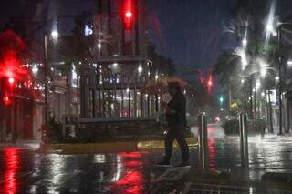Mulher tenta se proteger da chuva no início da manhã escura no Centro da Capital. (Foto: Henrique Kawaminami)