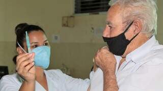 Profissional da saúde mostra seringa para idoso após vacina ser aplicada. (Foto: PMCG)