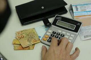 Com ajuda de calculadora, mulher faz as contas do que precisa pagar (Foto: Arquivo/Kisie Ainoã)