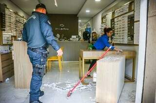 Policial militar no local enquanto fucionária faz a limpeza para abrir a loja. (Foto: Henrique Kawaminami)