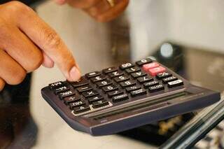 Pessoa usando calculadora para somar dívidas (Foto: Henrique Kawaminami | Arquivo)