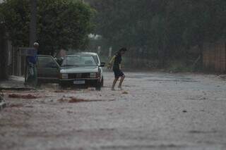 Moradora tenta atravessar a rua durante dia de chuvas intensas, em Campo Grande. (Foto: Henrique Kawaminami)