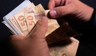 Beneficiário conta notas de dinheiro após efetuar o saque (Foto: Divulgação)