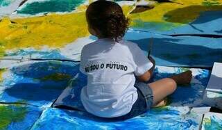 Criança sentada em desenhos com tinta. (Foto: Wilson Dias/Agência Brasil) 