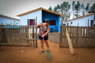 Moradora beneficiada limpando a frente de sua nova residência. (Foto: Divulgação) 