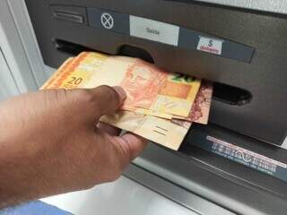 Homem saca dinheiro de caixa eletrônico. (Foto: Kísie Ainoã / Arquivo)