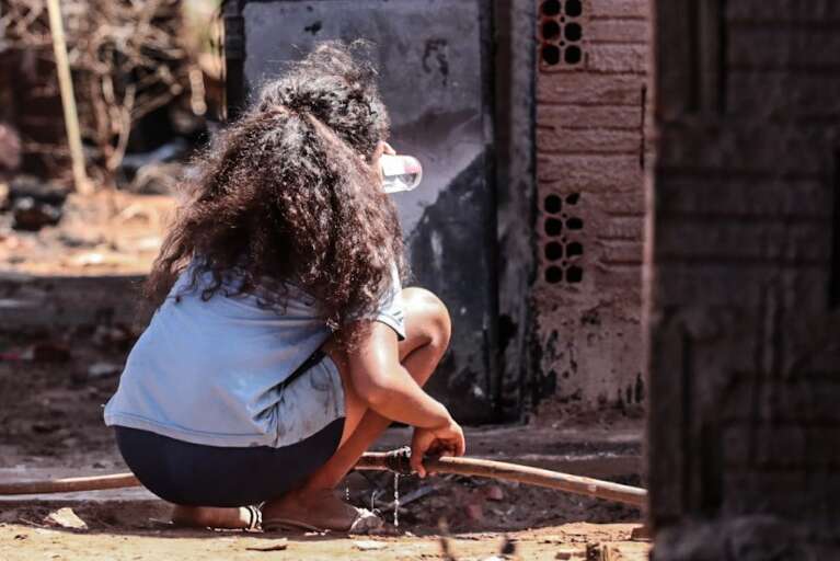 Filha de Adriana tomando água em furo de encanamento improvisado. (Foto: Marcos Maluf)