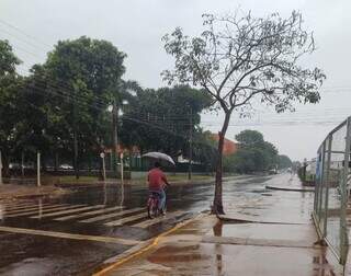 Morador da Vila Industrial enfrenta chuva desta manhã em Dourados (Foto: Helio de Freitas)