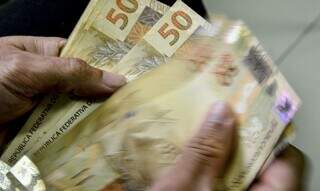Homem conta notas de R$ 50 após efetuar saque (Foto: Agência Brasil)