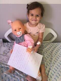Cecília com cartinha feita por enfermeira e a boneca parceira de hospital.