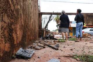 Muro destruído e moradora no local nesta manhã. (Foto: Henrique Kawaminami)