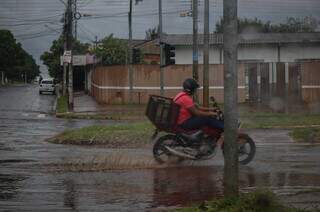Em dia de chuva, homem pilota motocicleta na Avenida Lúdio Martins Coelho, em Campo Grande. (Foto: Henrique Kawaminami)