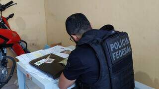 Policial relacionando documentos apreendidos durante a operação. (Foto: Divulgação | PF)
