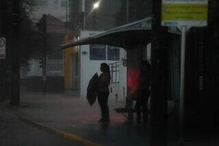 Mulher ewm ponto de ônibus enfrentando escuridão nesta manhã em Campo Grande. (Foto: Marcos Maluf)