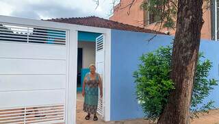 Dona Carmem abre o portão da casa nova, azul da cor da paz que ela buscava há tempos. (Foto: Ângela Kempfer)
