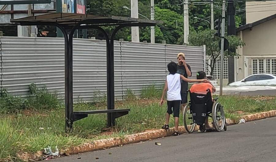 Sem calçada rebaixada, cadeirante espera ônibus na beira da rua
