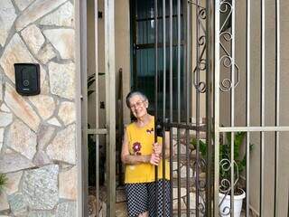 Olga sorridente no portão de ferro que dá acesso à casa. (Foto: Jéssica Fernandes)