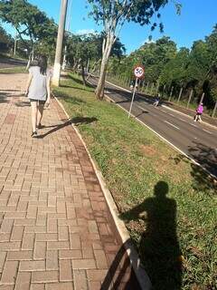 Mulher caminha na ciclovia, enquanto ciclista (sombra) aguarda. (Foto: Direto das Ruas)