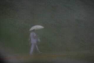 Mulher com guarda-chuva caminha em rua do bairro Chácara Cachoeira esta manhã. (Foto: Henrique Kawaminami)
