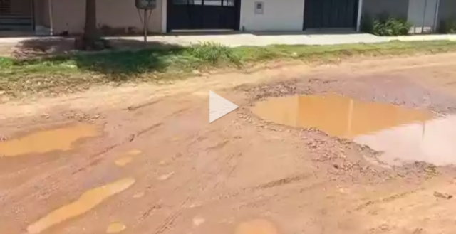 Em rua alagada e esburacada, motoristas trafegam na cal&ccedil;ada