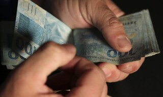 Homem realiza contagem das cédulas de R$ 100. (Foto: José Cruz/Agência Brasil)