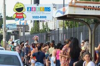 Pessoas, em pé, enfrentam fila, em frente à AACC para garantir vaga em bazar (Foto: Henrique Kawaminami)